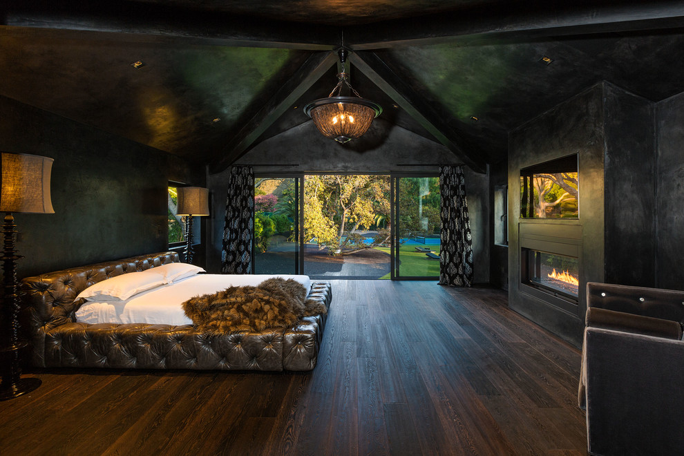 Imagen de dormitorio principal actual con paredes negras, suelo de madera oscura, chimenea lineal, marco de chimenea de hormigón y suelo marrón