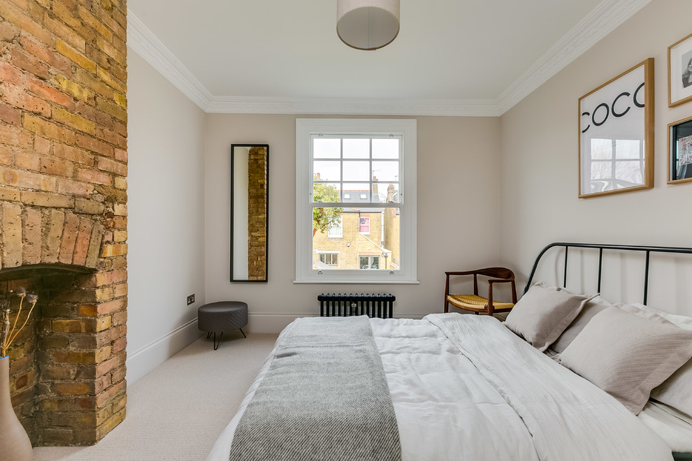 Medium sized scandinavian master bedroom in London with beige walls, carpet, beige floors, a standard fireplace and a brick fireplace surround.