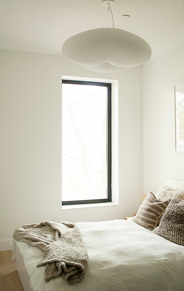 Design ideas for a small modern guest bedroom in New York with white walls and light hardwood flooring.