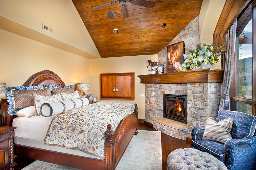Inspiration för ett rustikt sovrum, med beige väggar, mellanmörkt trägolv, en spiselkrans i sten och en öppen hörnspis