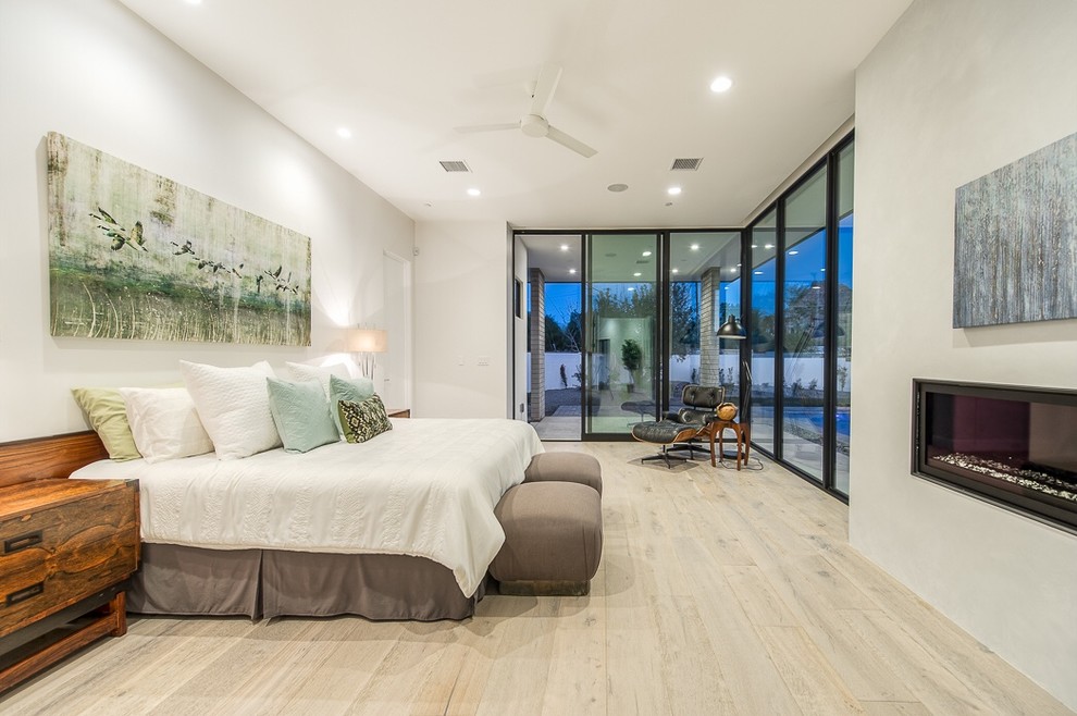Großes Modernes Schlafzimmer mit weißer Wandfarbe, hellem Holzboden und Gaskamin in Phoenix