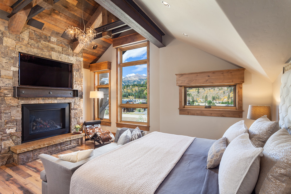 Aménagement d'une chambre parentale montagne avec un sol en bois brun, une cheminée standard et un manteau de cheminée en pierre.