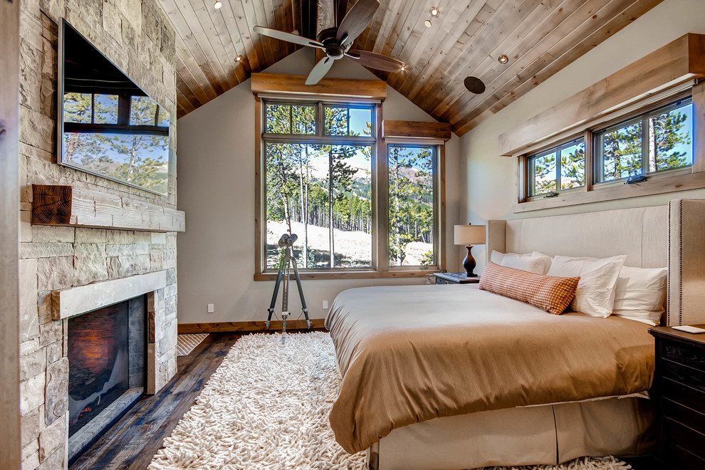 Rustikales Schlafzimmer mit beiger Wandfarbe, dunklem Holzboden, Kamin und Kaminumrandung aus Stein in Denver