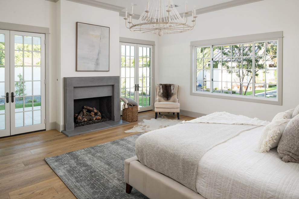 Imagen de dormitorio principal campestre grande con paredes blancas, suelo de madera clara, todas las chimeneas y marco de chimenea de hormigón