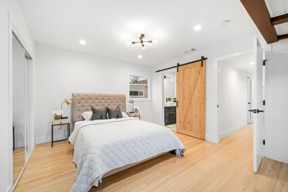 Ejemplo de dormitorio principal de estilo americano de tamaño medio con paredes blancas y suelo de madera clara