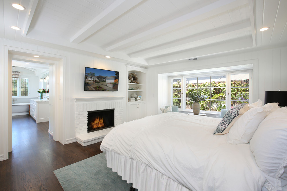 This is an example of a nautical master bedroom in Orange County with white walls, dark hardwood flooring, a standard fireplace and a brick fireplace surround.
