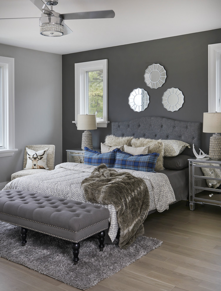 Exemple d'une grande chambre parentale tendance avec un mur gris, parquet clair, une cheminée d'angle et un manteau de cheminée en pierre.
