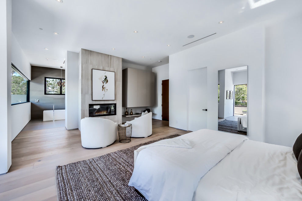 Großes Modernes Hauptschlafzimmer mit weißer Wandfarbe, hellem Holzboden, gefliester Kaminumrandung und Kamin in Los Angeles