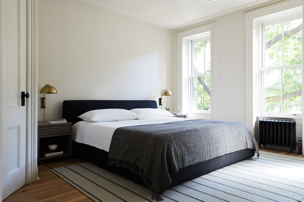 This is an example of a traditional master and cream and black bedroom in New York with white walls and light hardwood flooring.