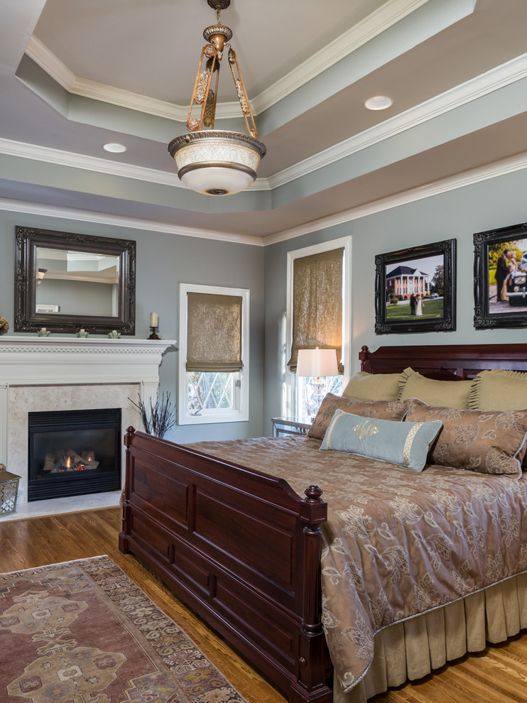 Imagen de dormitorio principal clásico de tamaño medio con paredes grises, suelo de madera en tonos medios, todas las chimeneas y marco de chimenea de madera