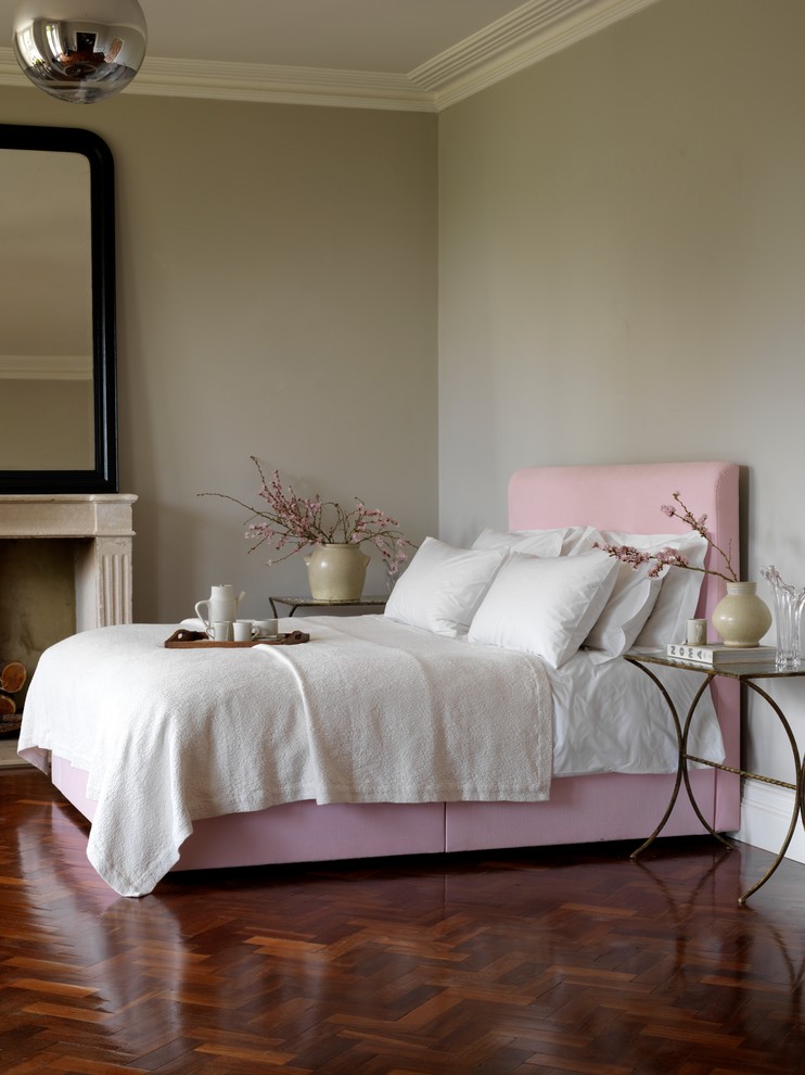 Photo of a world-inspired bedroom in London with grey walls, medium hardwood flooring and a standard fireplace.