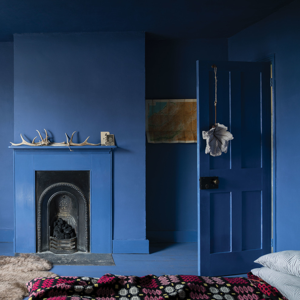 Eklektisk inredning av ett sovrum, med blå väggar, målat trägolv, en standard öppen spis och blått golv