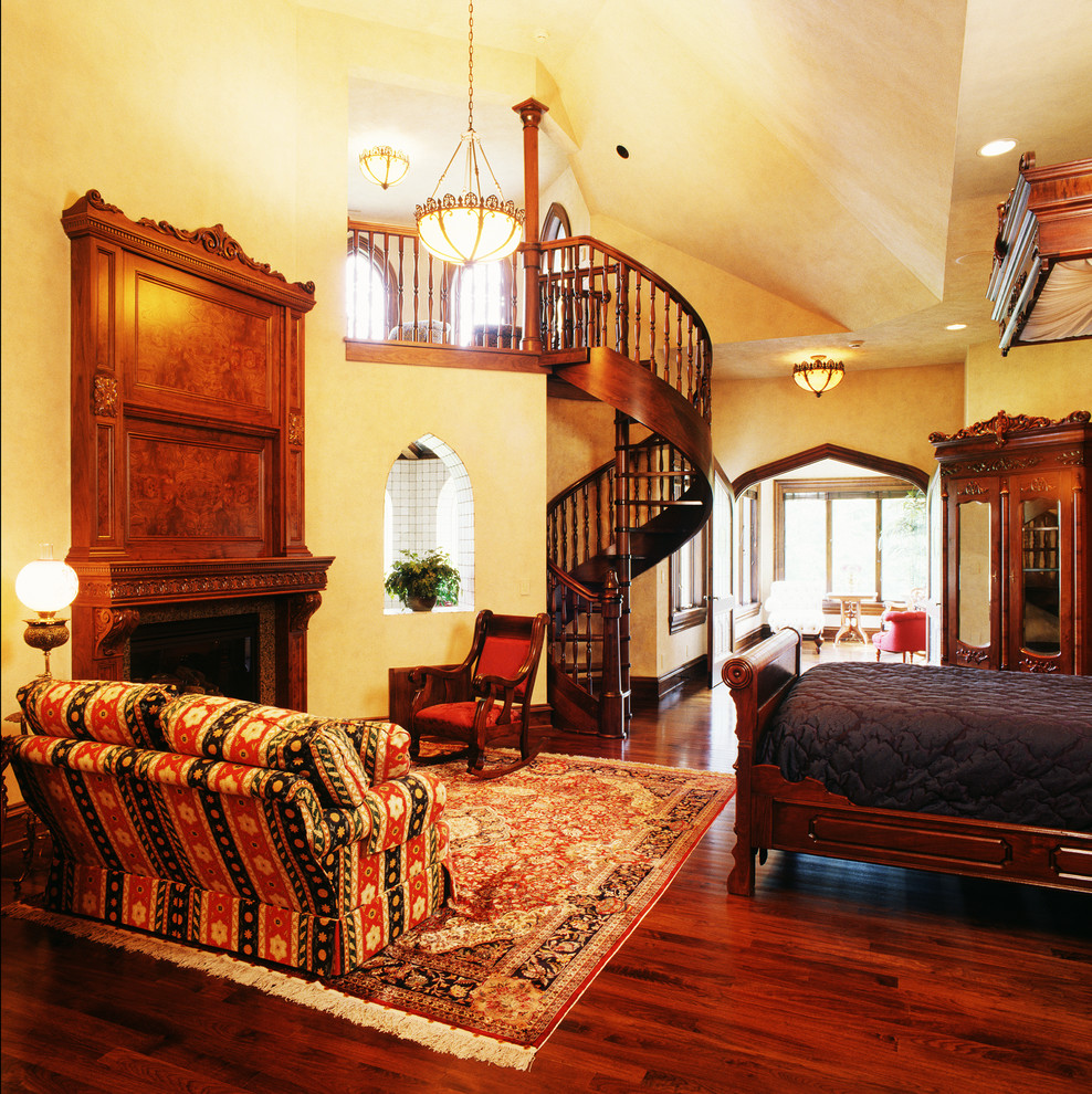 Geräumiges Mediterranes Hauptschlafzimmer mit beiger Wandfarbe, dunklem Holzboden, Kamin und Kaminumrandung aus Holz in Cedar Rapids