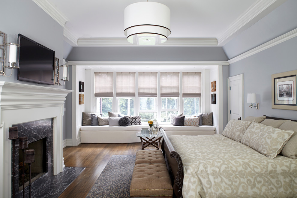 Example of a large classic master medium tone wood floor bedroom design in New York with gray walls and a standard fireplace