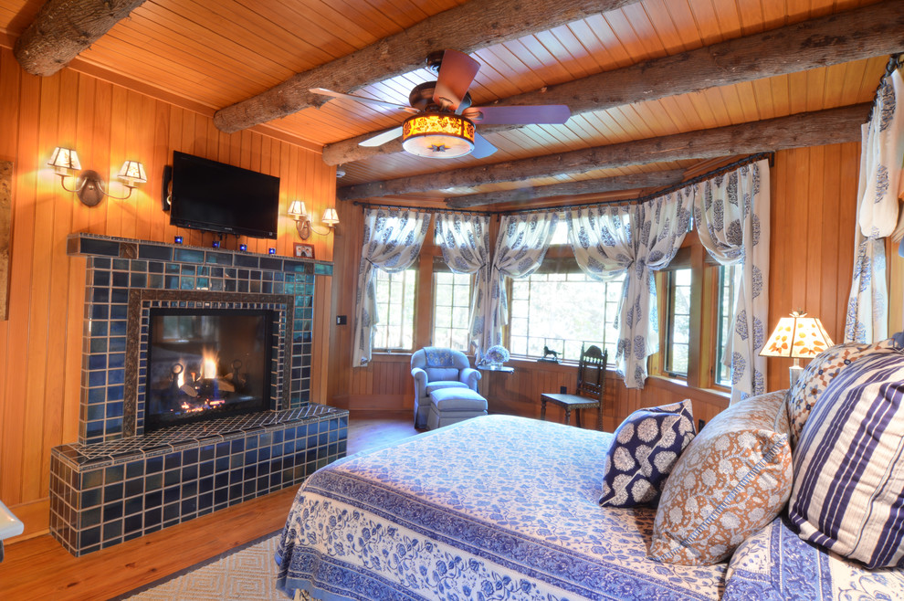 Imagen de dormitorio principal rural de tamaño medio con suelo de madera en tonos medios, todas las chimeneas y marco de chimenea de baldosas y/o azulejos