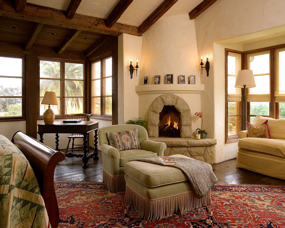 Geräumiges Mediterranes Hauptschlafzimmer mit Eckkamin, beiger Wandfarbe, dunklem Holzboden und Kaminumrandung aus Stein in Santa Barbara