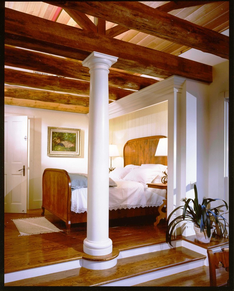 Immagine di una grande camera matrimoniale tradizionale con pareti bianche, pavimento in legno massello medio, camino classico e cornice del camino in pietra