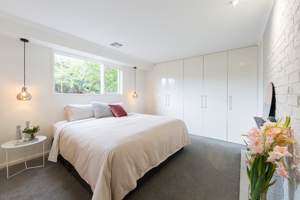Modelo de dormitorio moderno con moqueta, paredes blancas, marco de chimenea de ladrillo y suelo gris
