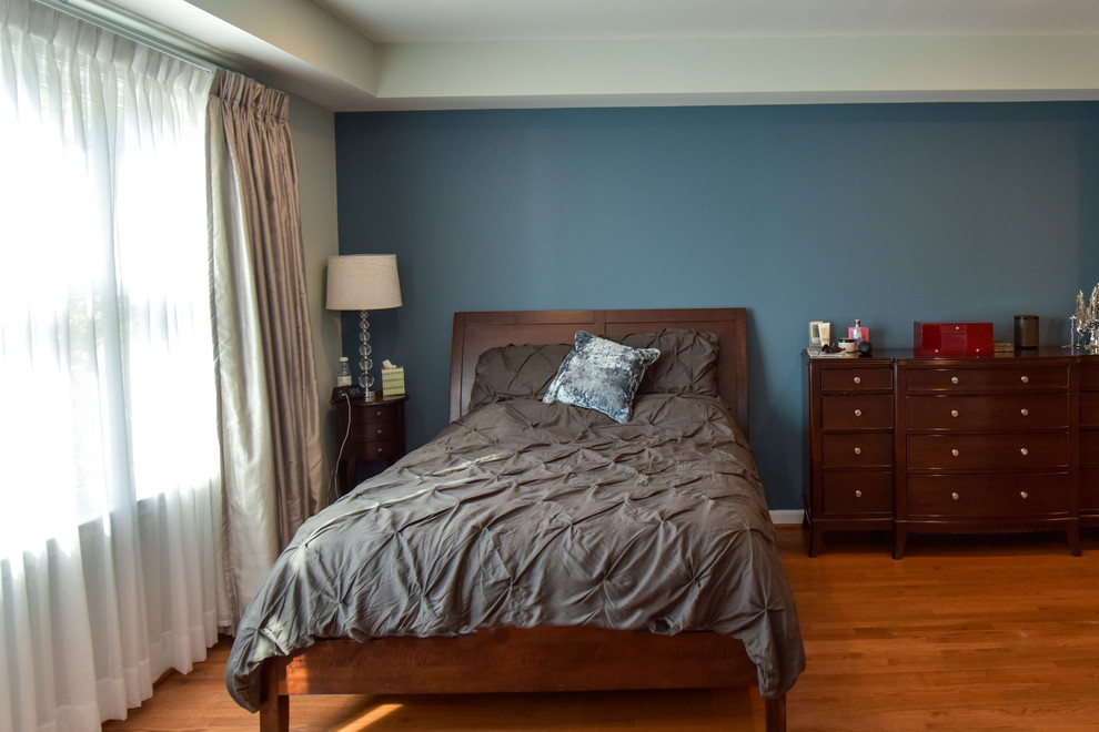 Cette image montre une grande chambre parentale traditionnelle avec un mur bleu, un sol en bois brun, cheminée suspendue, un manteau de cheminée en métal et un sol marron.