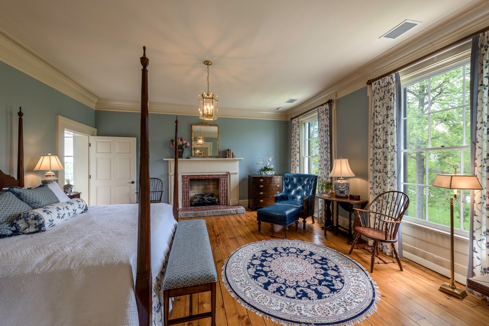 Imagen de dormitorio principal clásico grande con paredes azules, suelo de madera en tonos medios, todas las chimeneas, marco de chimenea de ladrillo y suelo marrón