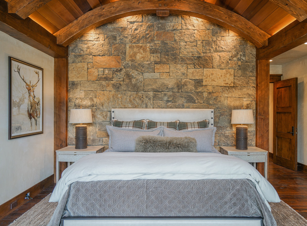 Großes Uriges Hauptschlafzimmer mit beiger Wandfarbe, dunklem Holzboden, Eckkamin und Kaminumrandung aus Stein in Denver