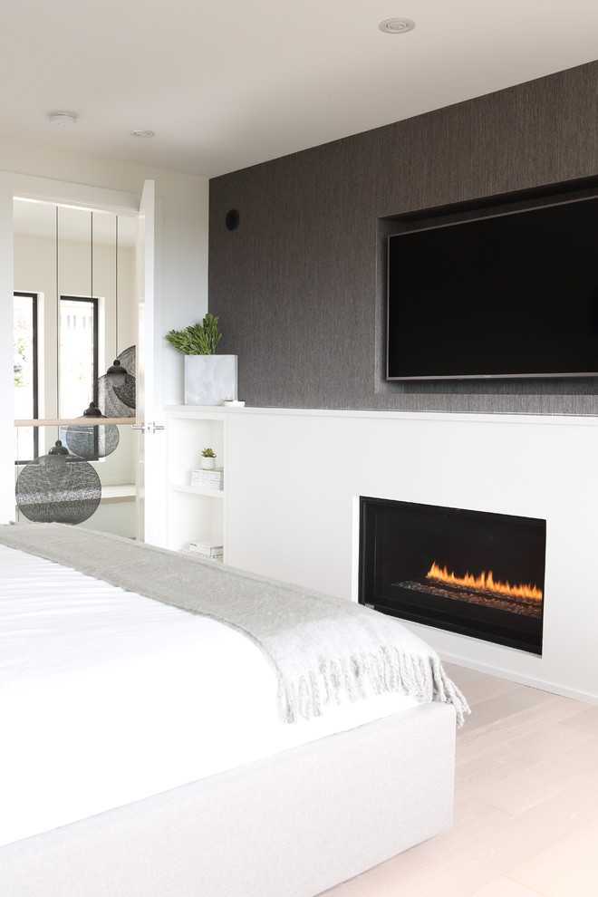 Example of a large trendy master light wood floor and beige floor bedroom design in Vancouver with white walls, a ribbon fireplace and a plaster fireplace