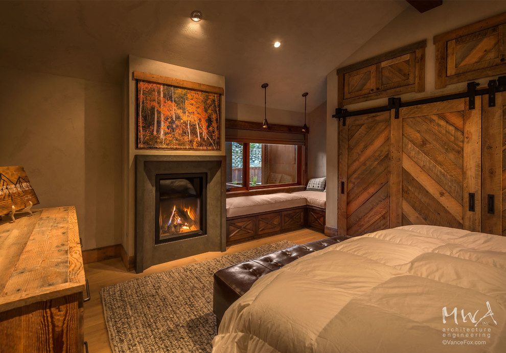 Cette image montre une grande chambre parentale chalet avec un mur beige, parquet clair, une cheminée standard et un manteau de cheminée en plâtre.