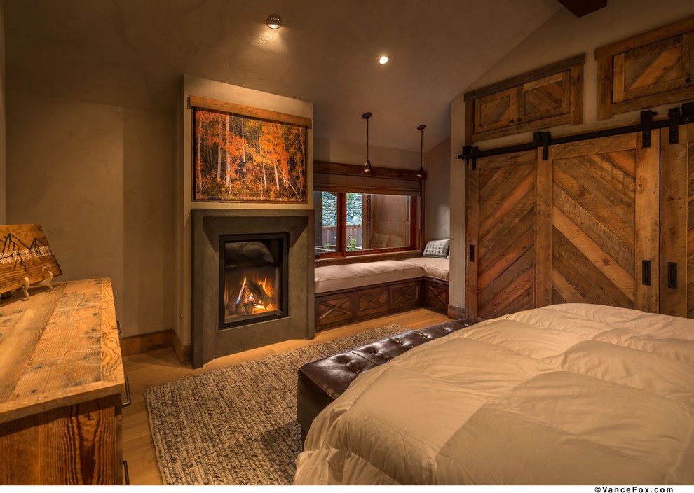 Ejemplo de dormitorio principal rural de tamaño medio con paredes grises, suelo de madera clara, todas las chimeneas y marco de chimenea de hormigón