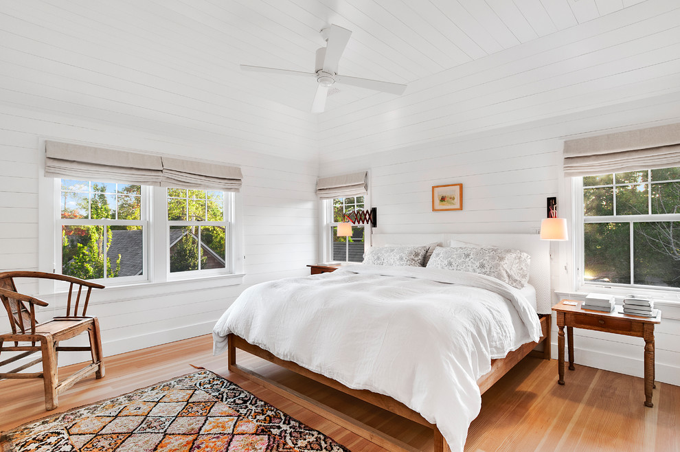 Modelo de dormitorio principal y blanco y madera costero grande con paredes blancas y suelo de madera clara