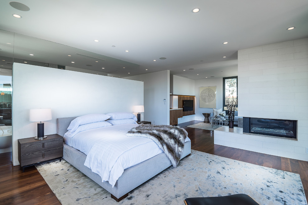 Стильный дизайн: хозяйская спальня среднего размера в стиле модернизм с белыми стенами, темным паркетным полом, горизонтальным камином и фасадом камина из камня - последний тренд