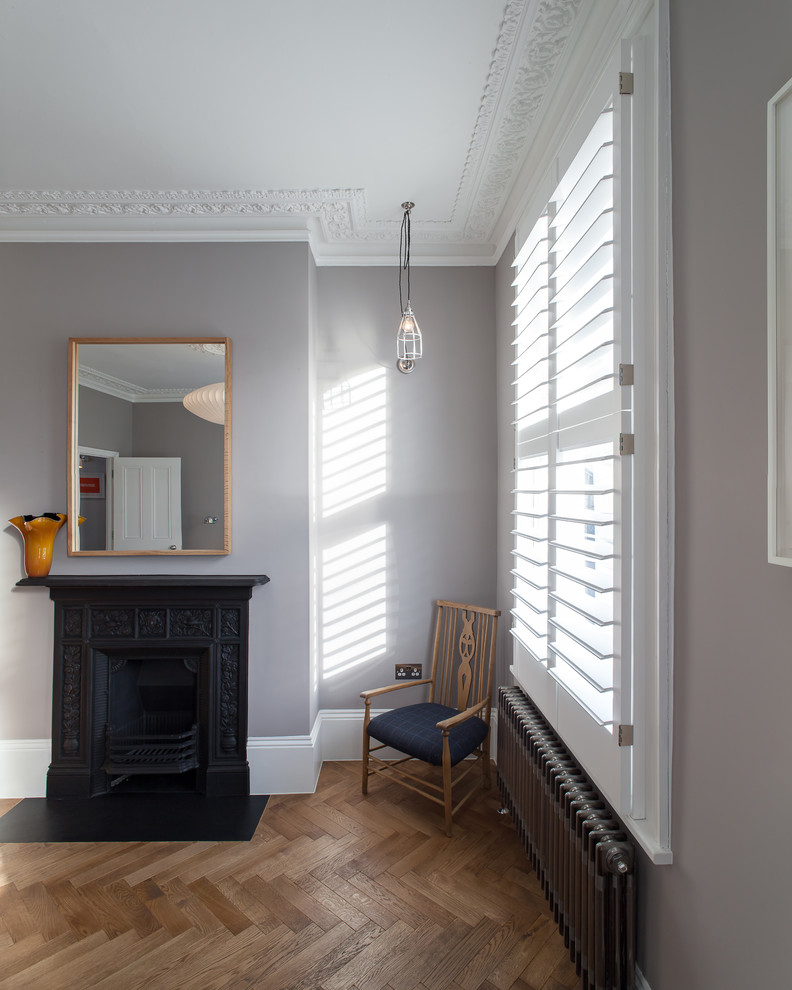 Mittelgroßes Modernes Hauptschlafzimmer mit grauer Wandfarbe, dunklem Holzboden, Kamin, Kaminumrandung aus Metall und braunem Boden in London