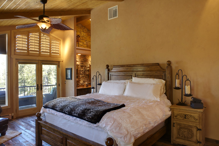 Exemple d'une grande chambre parentale sud-ouest américain avec un mur beige, parquet foncé, une cheminée standard et un manteau de cheminée en pierre.