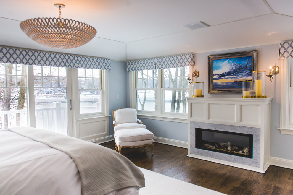 Foto de dormitorio principal clásico renovado grande con paredes azules, suelo de madera oscura, chimenea lineal y marco de chimenea de piedra