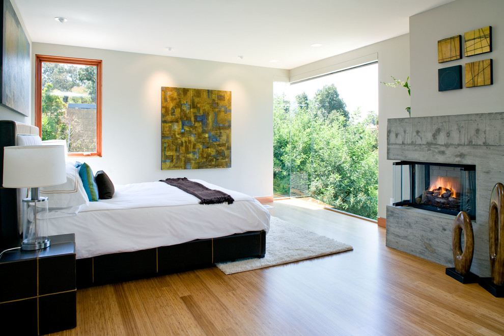 На фото: большая хозяйская спальня в современном стиле с белыми стенами, полом из бамбука, угловым камином и фасадом камина из бетона с