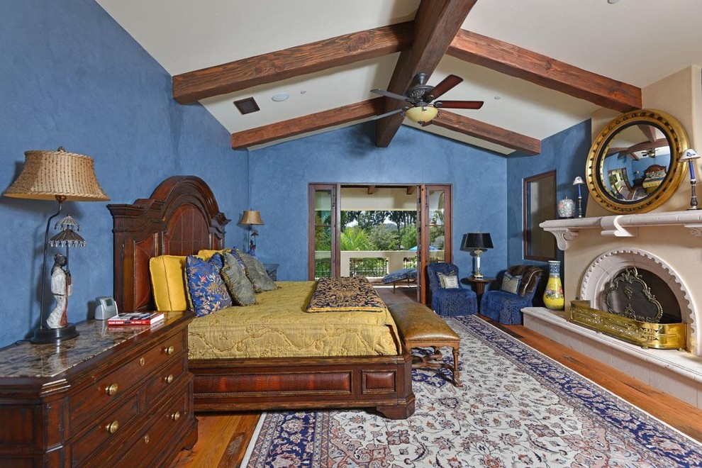 Mediterranes Hauptschlafzimmer mit blauer Wandfarbe, braunem Holzboden und Kamin in Sonstige