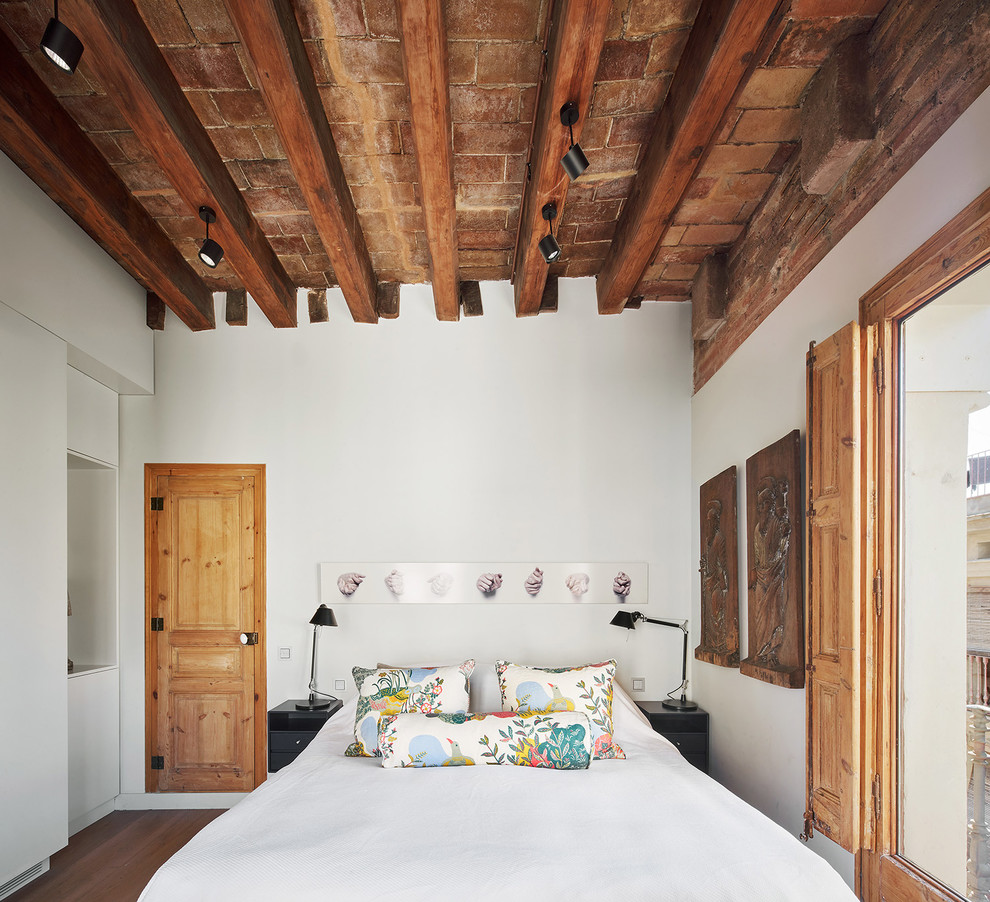 Ejemplo de dormitorio principal ecléctico con paredes blancas y suelo de madera en tonos medios