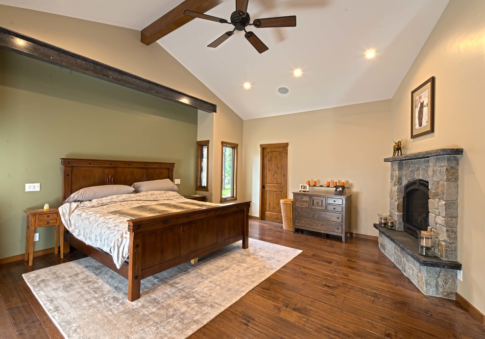 Imagen de dormitorio principal de estilo americano grande con paredes beige, suelo de madera oscura, todas las chimeneas, marco de chimenea de piedra y suelo marrón