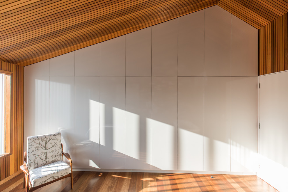 Modelo de dormitorio principal de tamaño medio sin chimenea con paredes blancas y suelo de madera en tonos medios