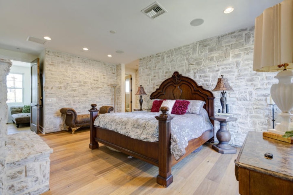 Foto de dormitorio principal campestre de tamaño medio con paredes blancas, suelo de madera clara, todas las chimeneas y marco de chimenea de piedra