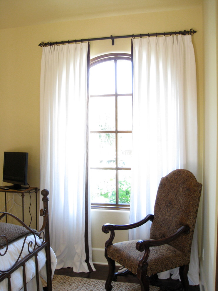 Ejemplo de habitación de invitados clásica de tamaño medio sin chimenea con paredes amarillas, suelo de madera oscura y suelo marrón