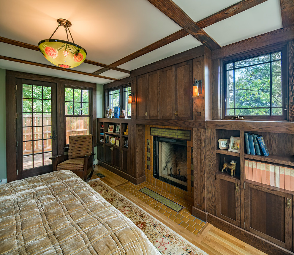 Diseño de dormitorio principal de estilo americano de tamaño medio con paredes verdes, suelo de madera clara, todas las chimeneas y marco de chimenea de baldosas y/o azulejos
