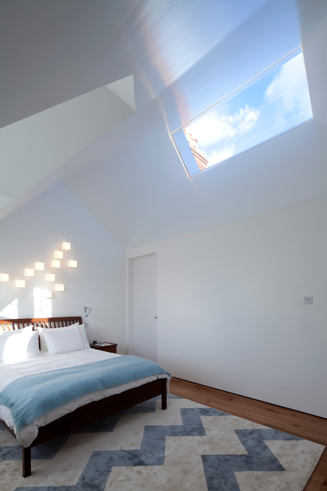 Design ideas for a large contemporary mezzanine bedroom in London with white walls and medium hardwood flooring.