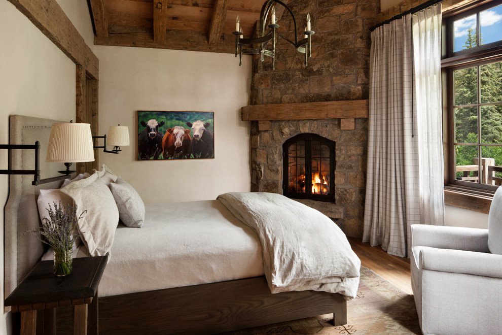 Idées déco pour une chambre d'amis montagne de taille moyenne avec un mur blanc, un sol en bois brun, une cheminée d'angle et un manteau de cheminée en pierre.