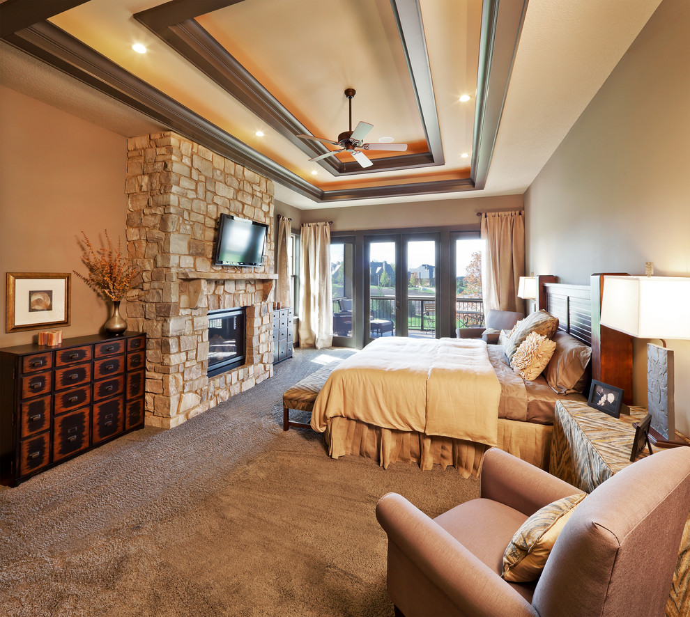 Modelo de dormitorio televisión rústico con paredes beige, moqueta, todas las chimeneas y marco de chimenea de piedra