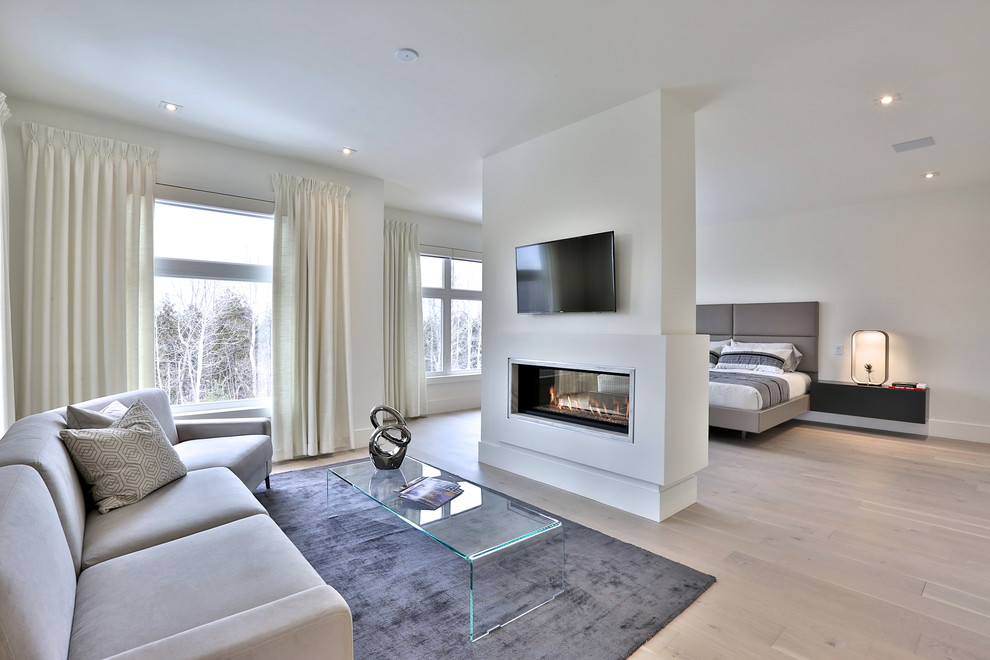 This is an example of an expansive modern master and grey and silver bedroom in Toronto with white walls, light hardwood flooring, a two-sided fireplace and a plastered fireplace surround.