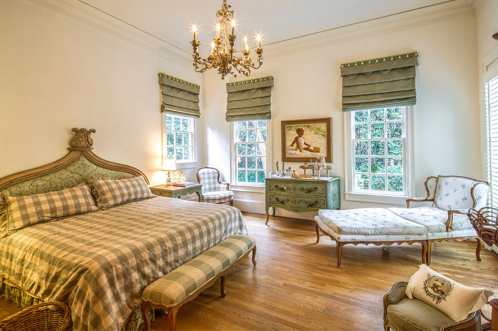 Ejemplo de dormitorio principal tradicional sin chimenea con suelo de madera en tonos medios y paredes blancas