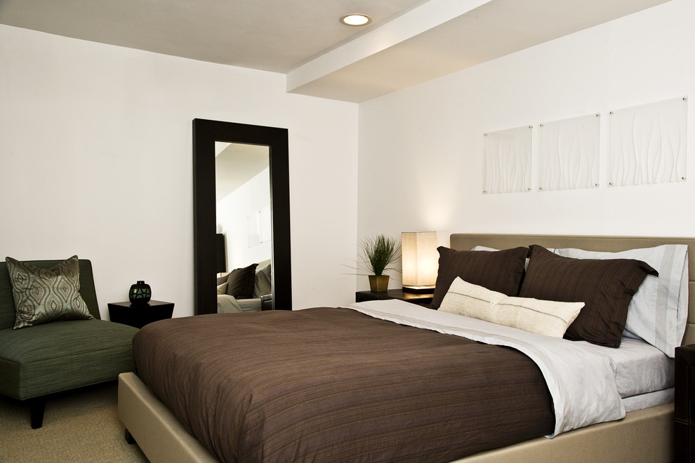 This is an example of a contemporary master bedroom in New York with white walls and carpet.