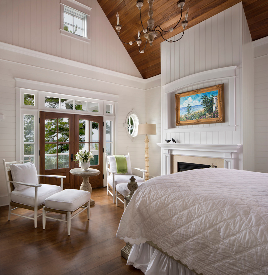 Cette photo montre une grande chambre parentale nature avec un mur blanc, un sol en bois brun, une cheminée standard et un manteau de cheminée en pierre.