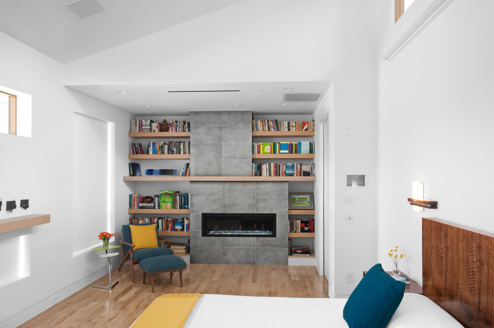 Modernes Schlafzimmer mit weißer Wandfarbe, hellem Holzboden, Kamin, Kaminumrandung aus Beton und beigem Boden in Houston