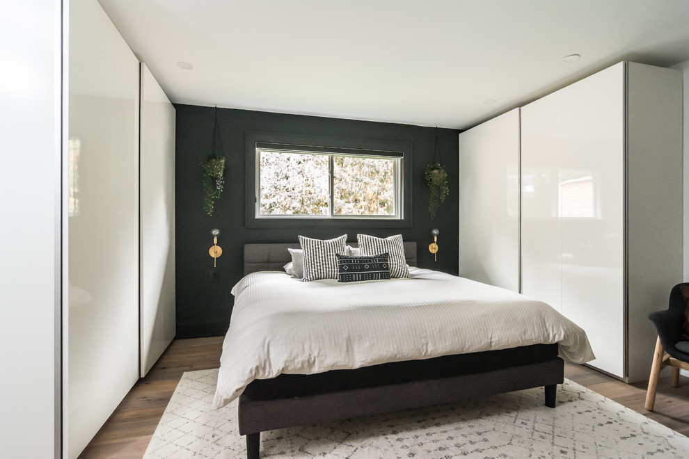 Large contemporary master bedroom in Toronto with brown floors, black walls and dark hardwood flooring.